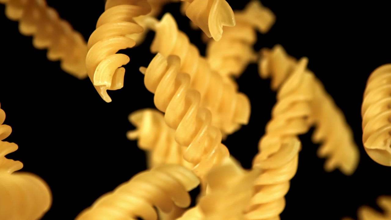 Pasta fusilli dorata che cade al rallentatore su sfondo nero
