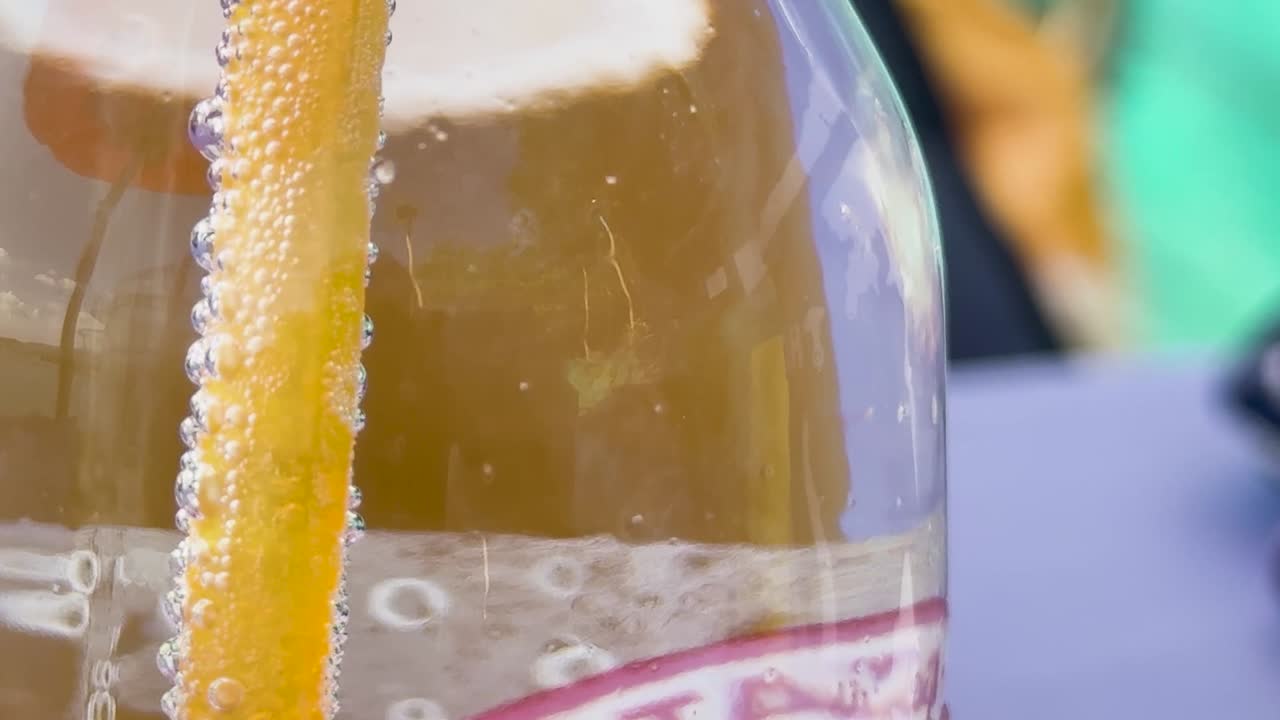 Close-up view of bubbles forming and rising along a yellow straw inside a transparent bottle.