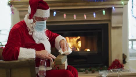 Papá-Noel-Con-Mascarilla-Desinfectando-La-Caja-De-Regalo-En-Casa