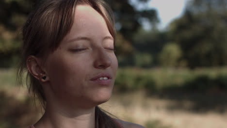 Close-up-of-a-young-woman-sitting-beneath-the-shade-of-the-tree-while-sun's-rays-falling-on-her-face