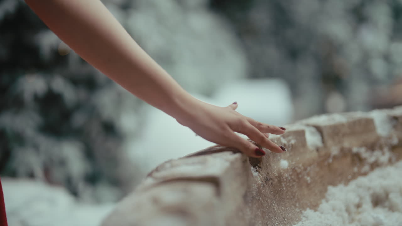A hand gently touches a snowy stone wall outdoors, evoking calm and winter peace