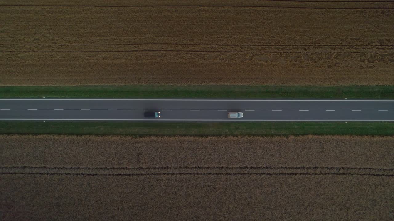 들판 사이의 직선 도로에서 헤드라이트를 켜고 지나가는 자동차