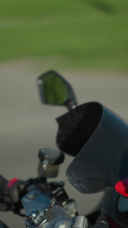 una vista de cerca de una motociclista femenina montando una bicicleta eléctrica roja, con una camisa a cuadros y zapatos de lona, casco puesto, un coche estacionado es débilmente visible en el fondo