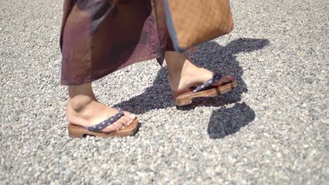 Side-angle-of-a-guy-wearing-a-yukata-wearing-traditional-wooden-sandles-walking-towards-a-temple-in-Kyoto,-Japan-soft-lighting