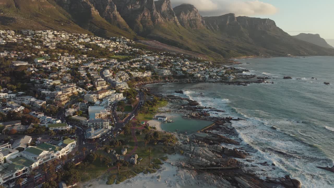 Drone flies over the camps bay in cape town south africa - many houses on a hillside - drone flies backwards over houses with view to table mountain and rocks in the sea