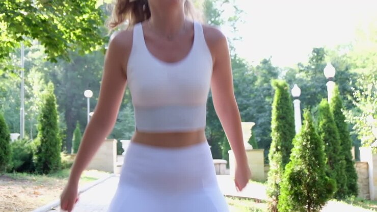 Donna bruna in abbigliamento sportivo bianco che si allena nel parco