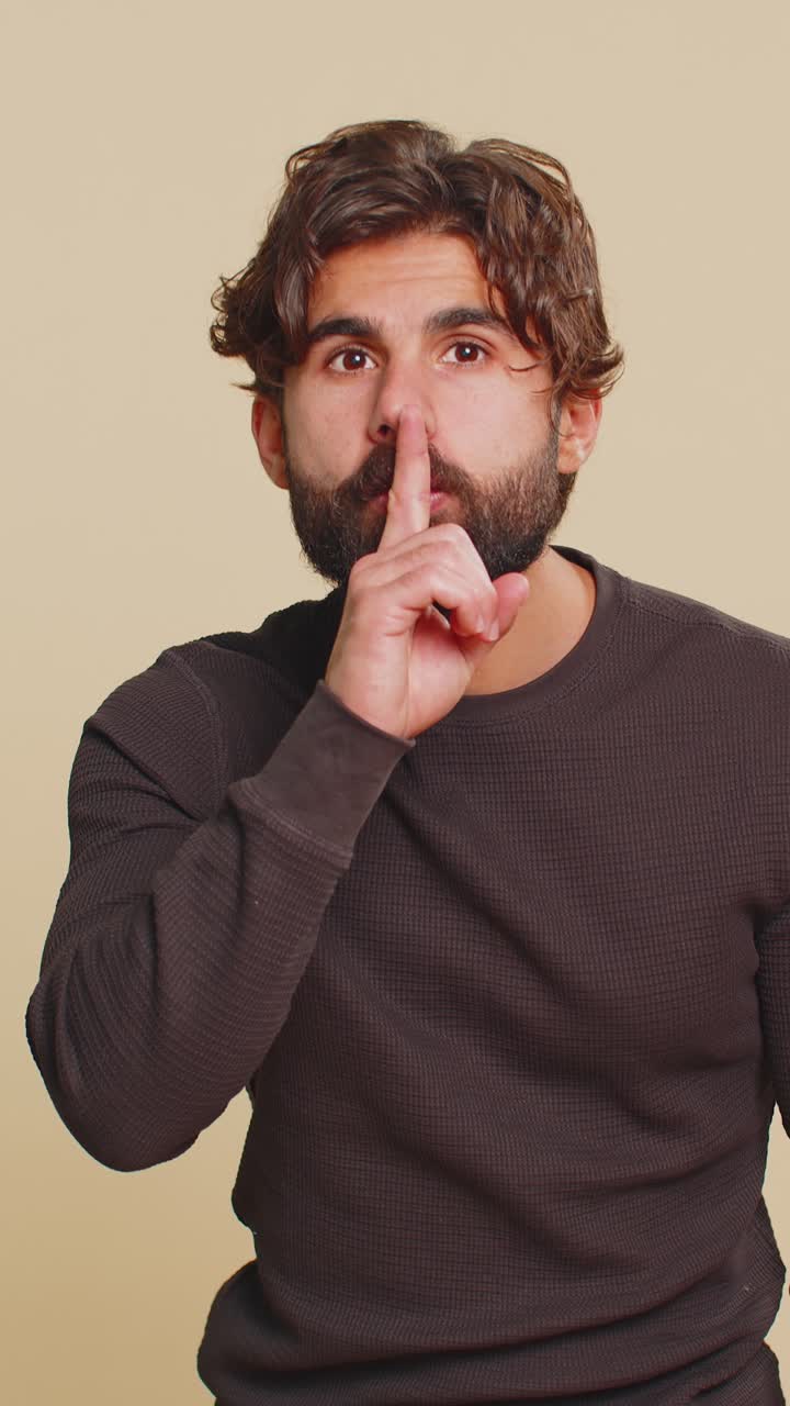 Giovane libanese preme l'indice sulle labbra e fa gesto di silenzio su sfondo beige in studio