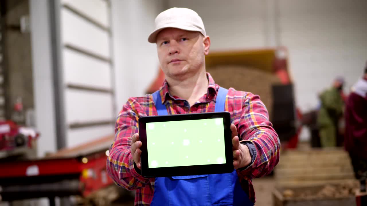el agricultor sostiene una tableta digital con pantalla verde en sus manos, en el fondo de un almacén de almacenamiento de patatas. agricultura, industria alimentaria, cosecha de patatas, agricultura