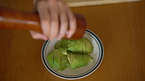 Close-up-of-man-grates-pepper-on-a-sliced-​​avocado-on-a-plate