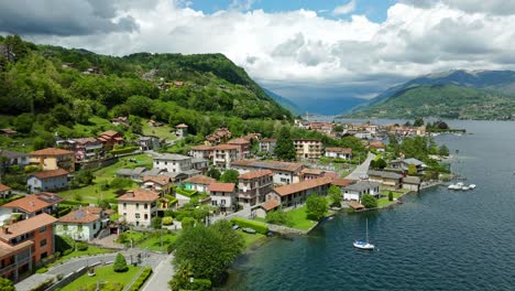 Aerial-View-Of-A-Picturesque-Waterfront-Town-With-Colorful-Buildings-Bordering-Pella-Lake,-Backed-By-Green-Hills-On-Sunny-Day