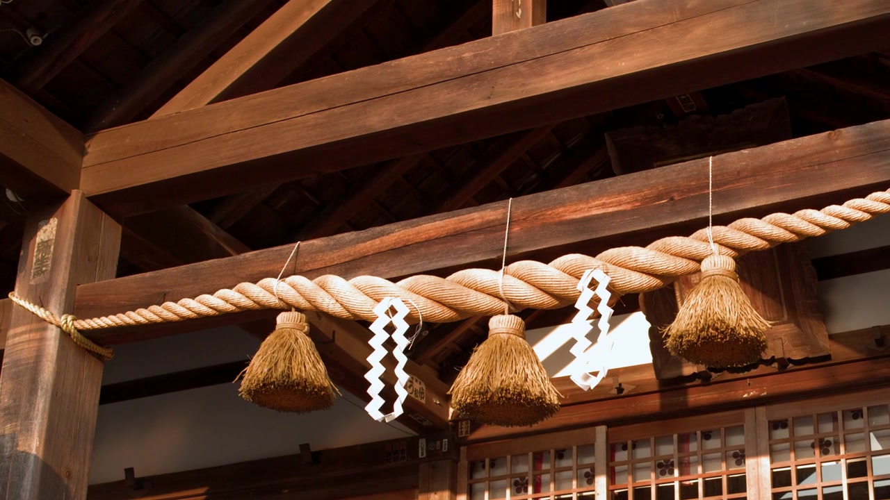 Primo piano di una sacra corda shimenawa con strisce di carta shide su un santuario shintoista di legno