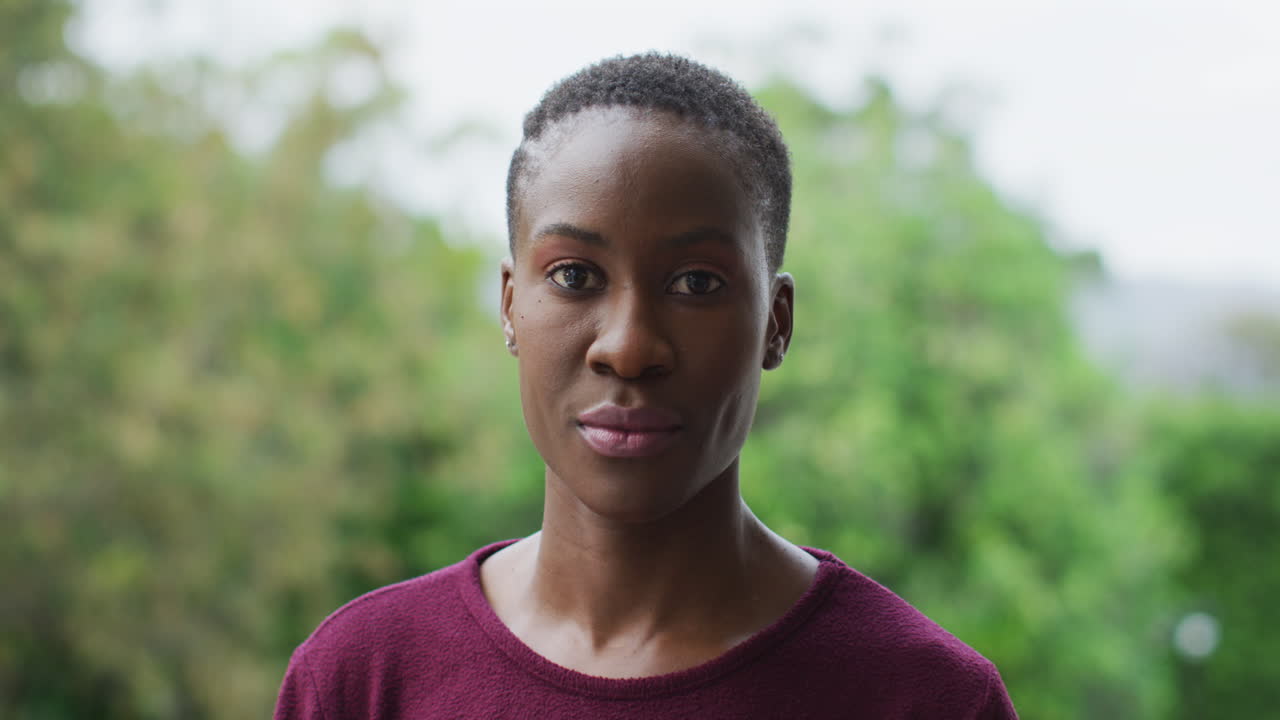mujer afroamericana de pie, sonriendo a la cámara al aire libre