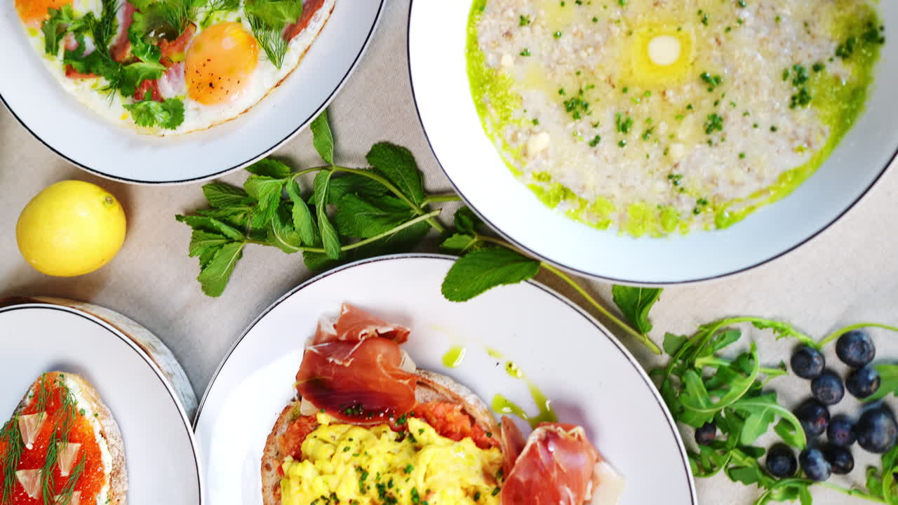 White plates displaying traditional Eastern European breakfast spread, scrambled eggs, prosciutto, caviar, pancakes, porridge, garnished with fresh seasonal berries