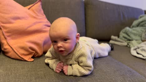 close up shot of cute young newborn baby lying on belly on couch at home - happy male baby inside living room - slow motion footage