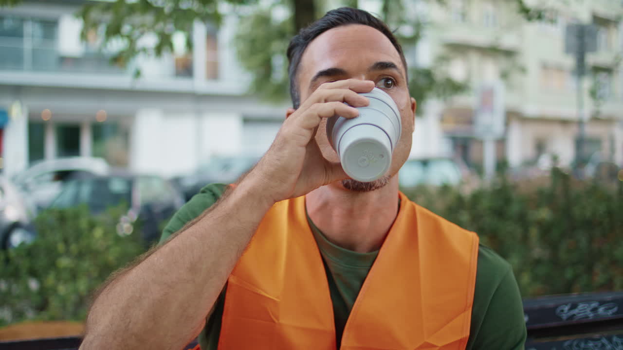 Construction worker sitting bench sipping coffee at street closeup. Man drinking