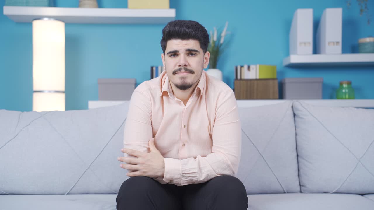 un joven de pensamiento negativo mirando a la cámara en casa.