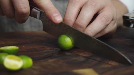 Slicing-green-lime-lemon-with-kitchen-knife-on-wooden-cut-board