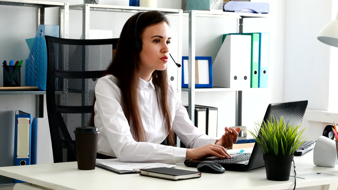 mujer hablando con auriculares y usando portátil en una oficina moderna
