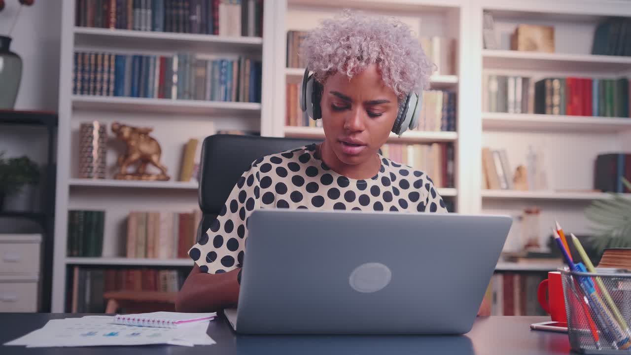 Woman listens to music in headphones at desk using laptop dancing in good mood