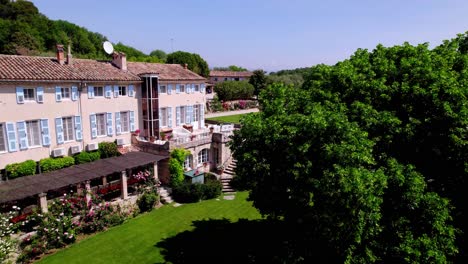 Drohne-Fliegt-Zu-Einem-Provenzalischen-Landhaus:-Blaue-Fensterläden,-Grüner-Rasen,-Rosengarten-Und-Blumenbeete