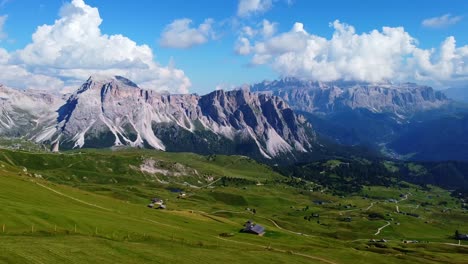 Vista-Aérea-De-La-Profundidad-De-Val-Gardena-En-Seceda-Con-Pastos-Verdes,-Senderos-Para-Caminatas-Y-Cabañas-En-Primer-Plano,-Y-Montañas-En-El-Fondo-En-Los-Dolomitas-Italianos-En-Tirol-Del-Sur,-Italia