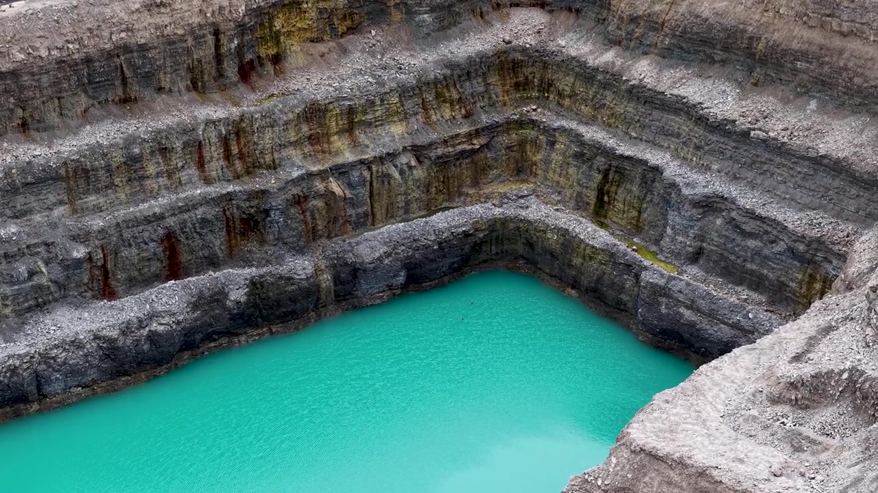Pemandangan drone melintasi air tambang pirus yang dibatasi oleh dinding batu kapur berlapis yang curam.