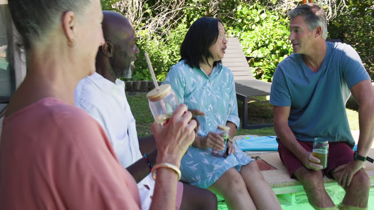 Diverse friends enjoying drinks and laughter in garden, sharing joyful moments together