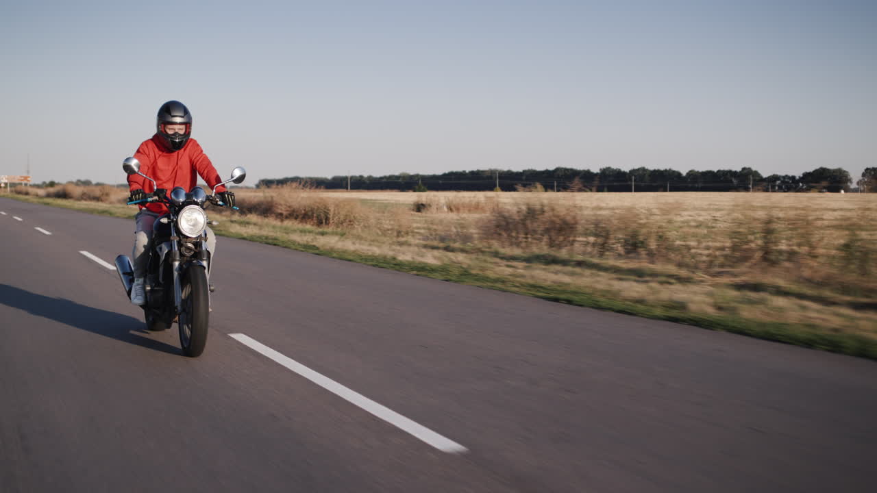 빨간 재킷을 입은 오토바이 운전자가 시골길을 달리다