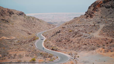 static wide shot of car driving on curvy road between rocky mountain of gran canaria