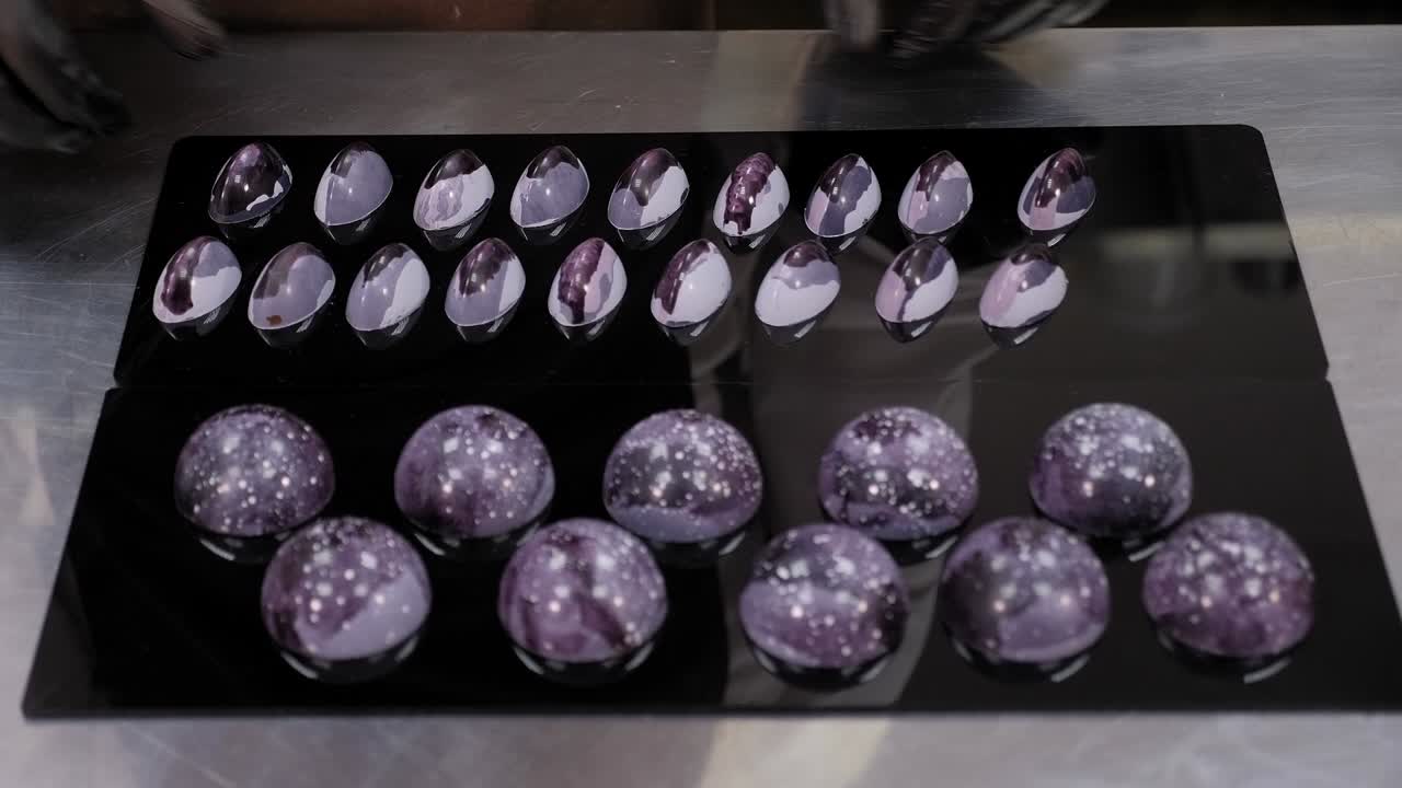 검은색 거울 표면에 색의 초콜릿을 놓고 있는 페이스트리 셰프의 클로즈업입니다.