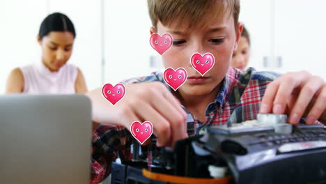 múltiples iconos de corazón rosa flotando sobre un niño caucásico reparando una computadora en la clase en la escuela