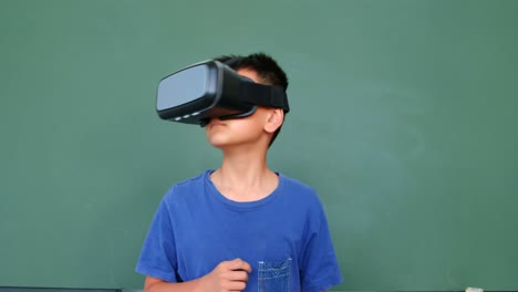 Vista-Frontal-De-Un-Colegial-Asiático-Usando-Auriculares-De-Realidad-Virtual-Contra-Una-Pizarra-Verde-En-El-Aula-4k