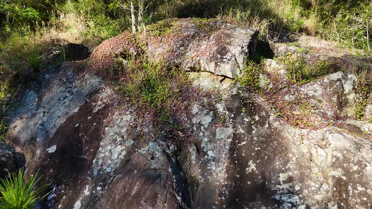 Aerial view of rocky landscape transitioning to lush greenery, captured in bright daylight with smooth camera movement
