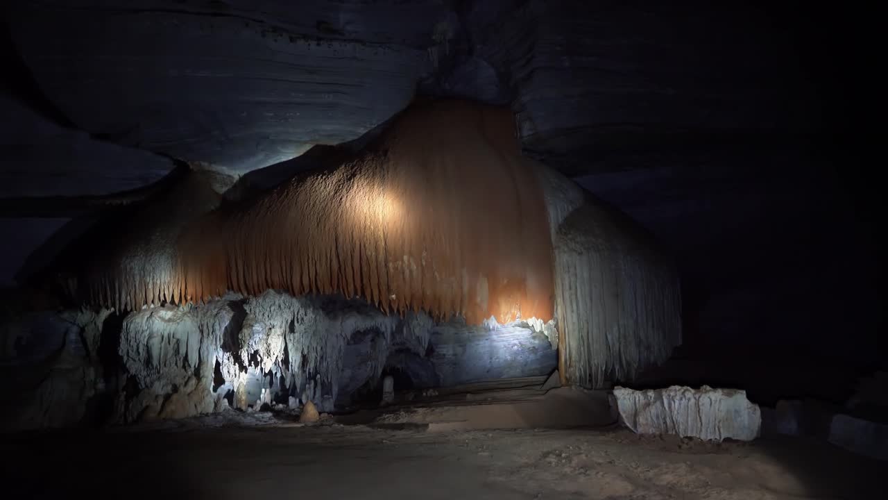 브라질 북동부 바히아의 차파다 디아만티나 국립공원에 있는 유명한 라파 도세 동굴 안에 있는 거대한 주황색과 흰색 동굴 구조를 비추는 손전등의 핸드헬드 샷