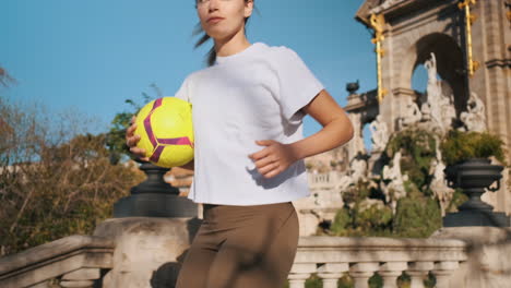 Sporty-woman-with-soccer-ball-in-hands-running-down-the-stairs-during-training-in-city-park.