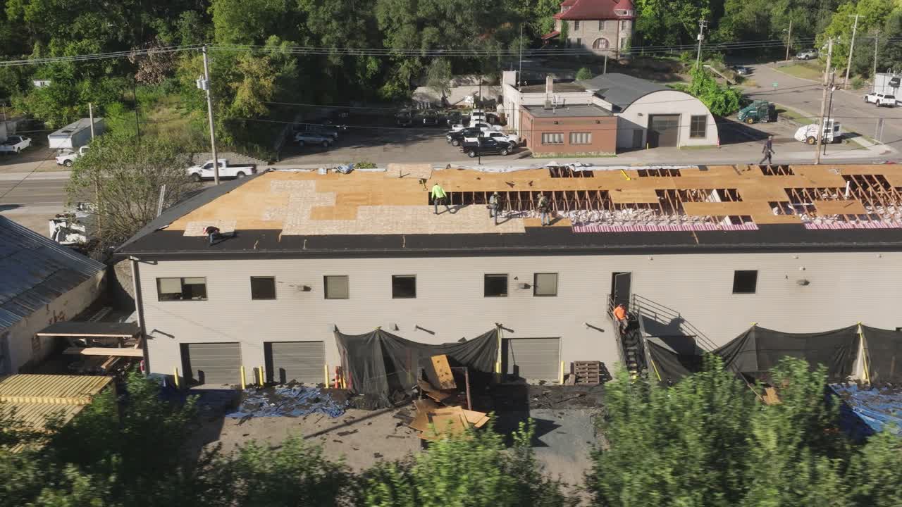 techadores reparando daños estructurales y reemplazando madera contrachapada en el techo de un gran edificio comercial.