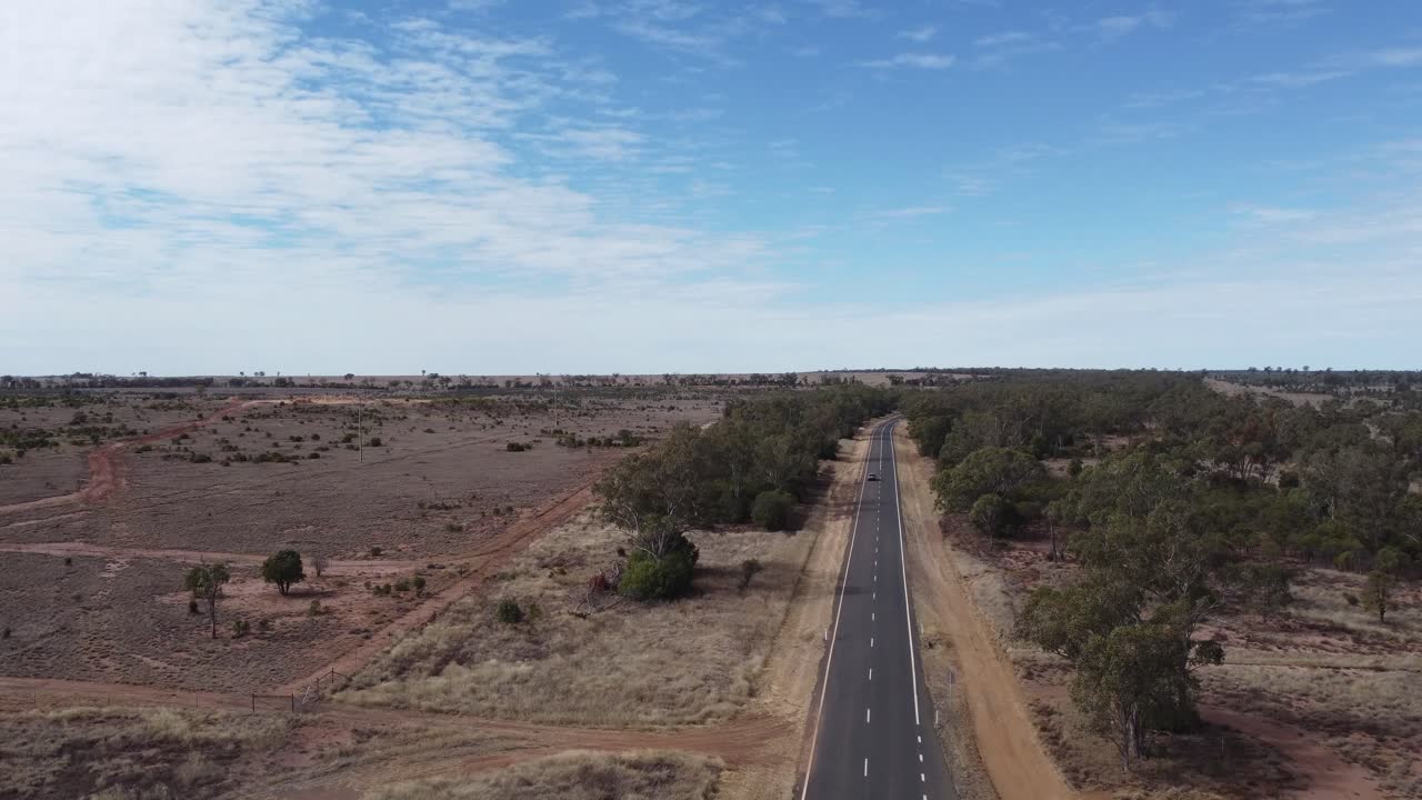drone ascendiendo sobre una carretera en un paisaje de estilo desierto un coche que pasa