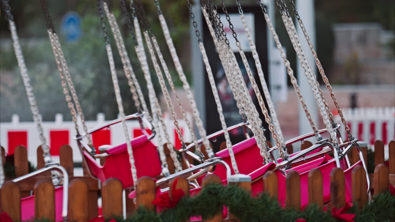 Festive amusement park swing ride with empty red chairs hanging from metal chains