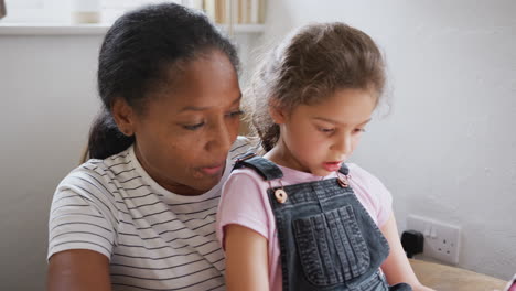 Grandmother-Sitting-In-Chair-With-Granddaughter-Using-Digital-Tablet-Together