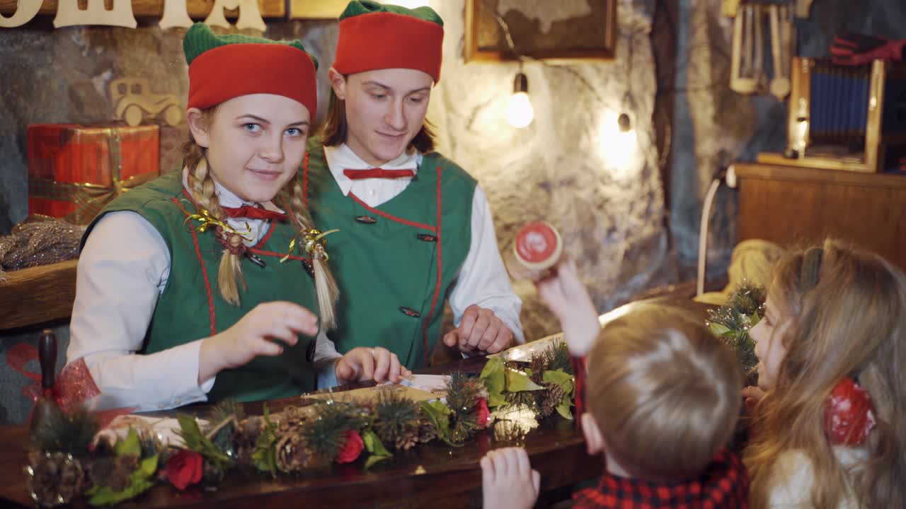Happy elves preparing letters with children. Elves and children making envelopes at Christmas