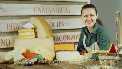 la amable vendedora sonriendo a la cámara parada detrás del mostrador con mucho queso