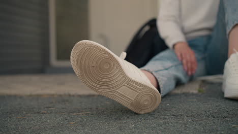 close-up of sneaker sole of seated individual, with hand resting on leg and black bag nearby, casual, outdoor setting conveys relaxed mood