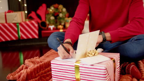 biracial man writing christmas greetings on christmas card at home, slow motion