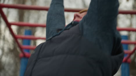 close-up of a coach exerting effort as he navigates across red iron bars, with a blurred background of bare trees