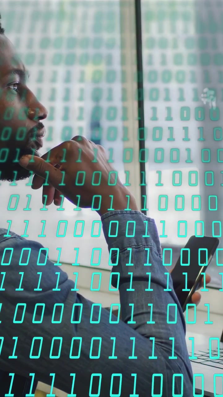 Vertical video: IT pro in office tapping phone, leaning, reviewing data, binary overlay on screen