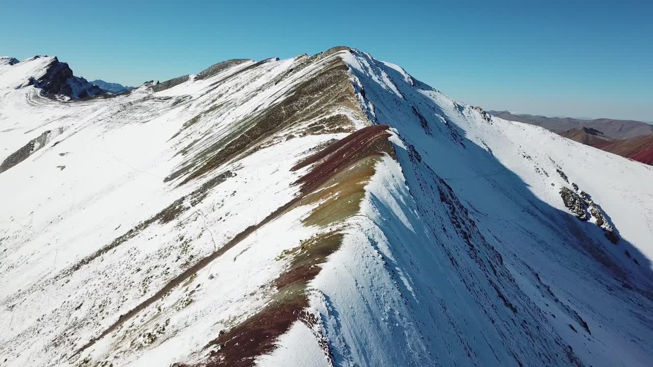 Aerial, tracking, drone shot overlooking snowy Vinicunca rainbow mountain, sunny day, in Pitumarca, Andes, Peru, South America