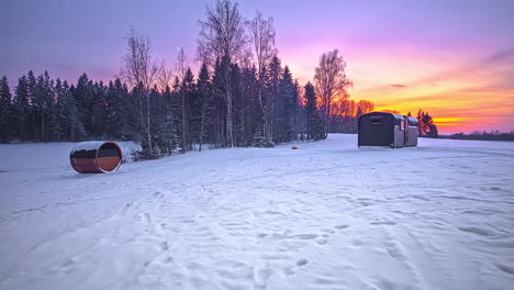 Wunderschöner-Tag-zu-Nacht-Zeitraffer-Der-Verschneiten-Winterlandschaft-Und-Des-Farbenfrohen-Himmels-Bei-Sonnenuntergang---Tannenbäume,-Barell-Sauna-Und-Holzhütte-Während-Des-Urlaubs-In-Nordeuropa