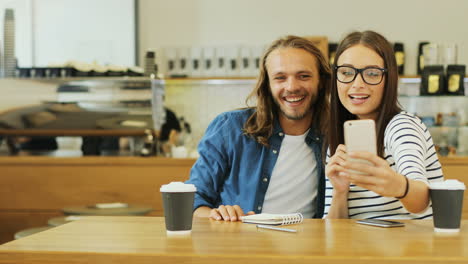 caucasian man and woman friends making a selfie using smartphone sitting at a table in a cafe