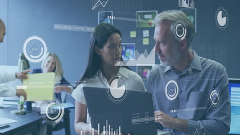 Business team collaborating around desk passing yellow folder and viewing laptop holographic charts