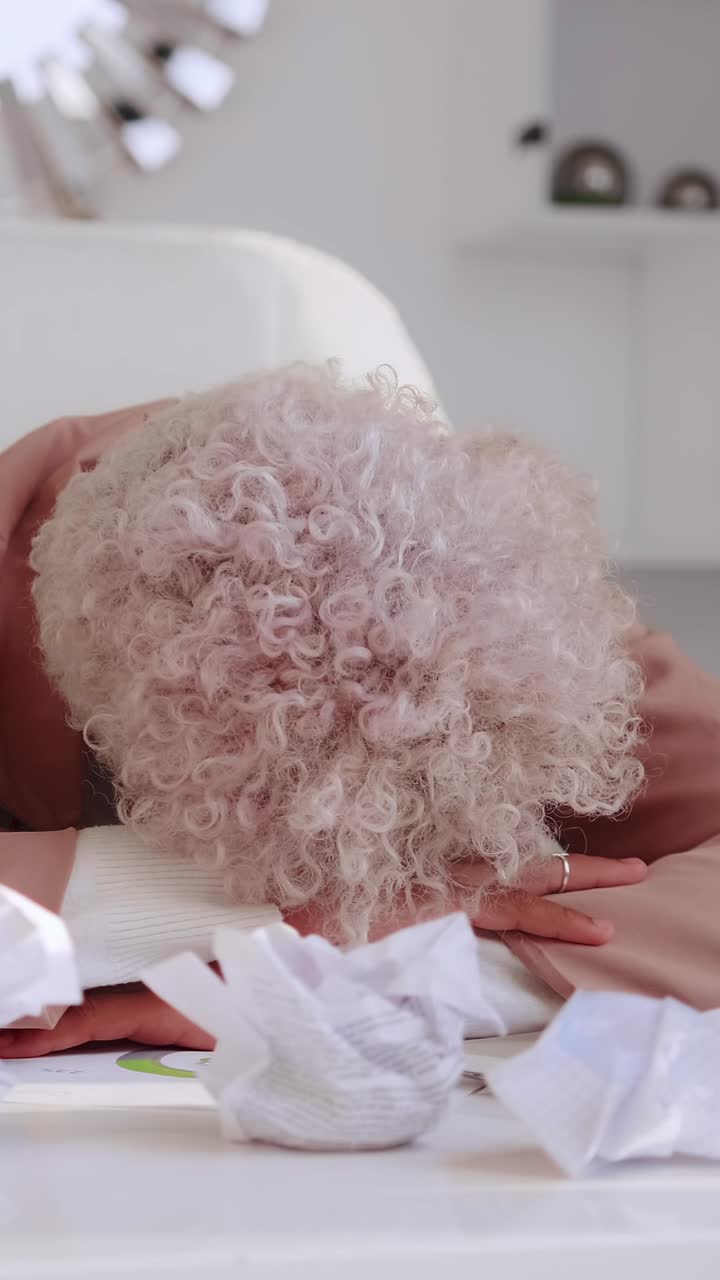 Tired frustrated woman yawns and covers mouth while sitting at a cluttered desk